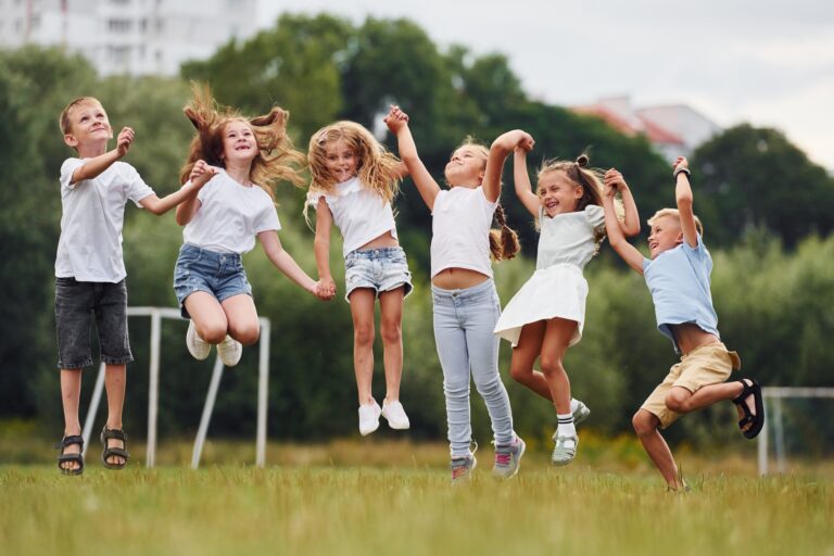 Holding each other by hands and jumping. Kids are having fun on the field at daytime together